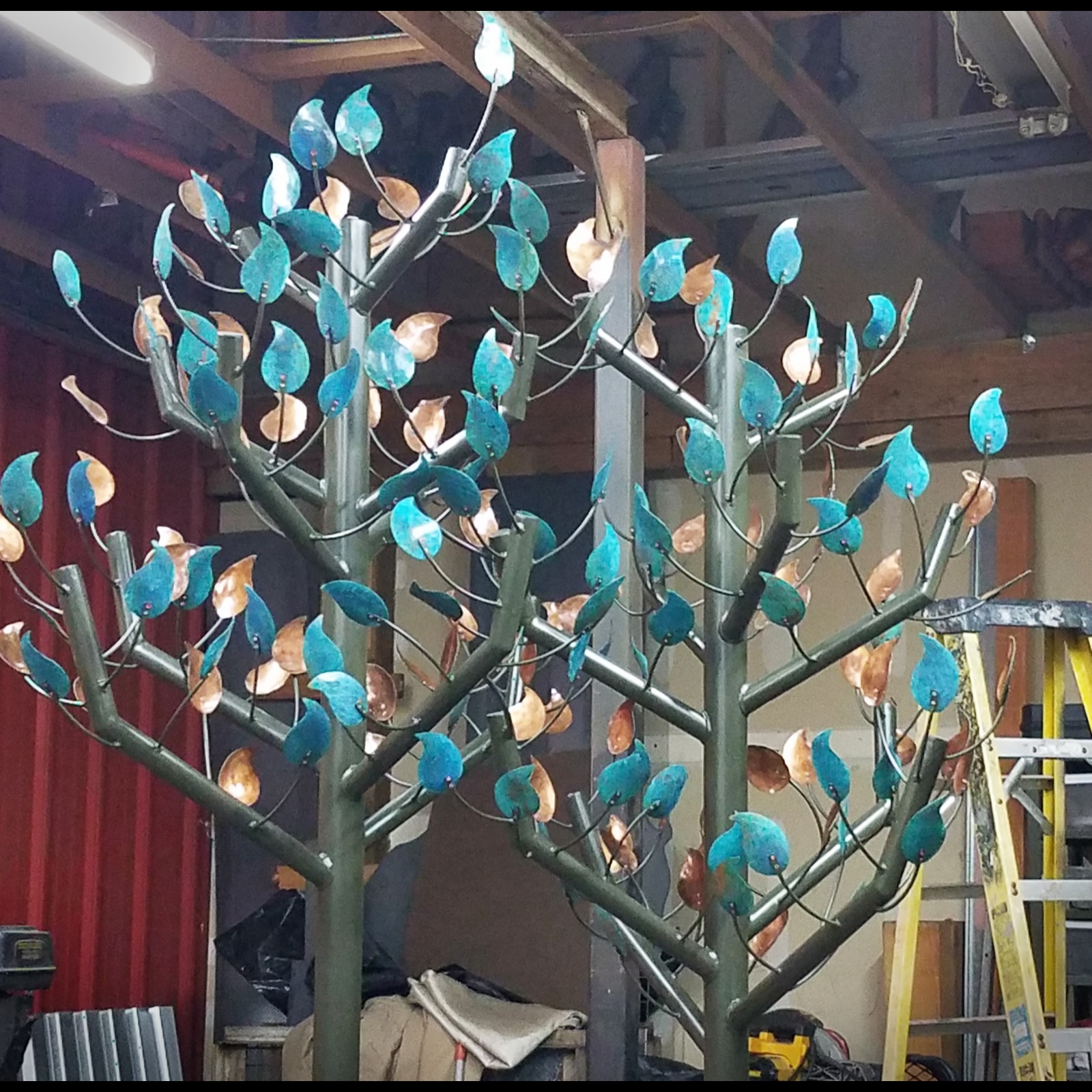 Two steel trees growing side by side, their branches full of turquoise and copper-colored leaves.